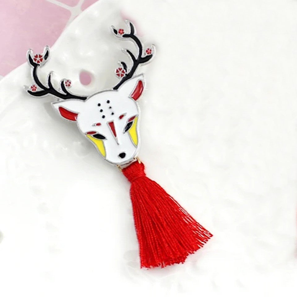 une broche en métal en forme d'un cerf représenté de façon onirique selon le folklore japonais. Il est élégant avec ces bois fleuris et son pompon rouge.