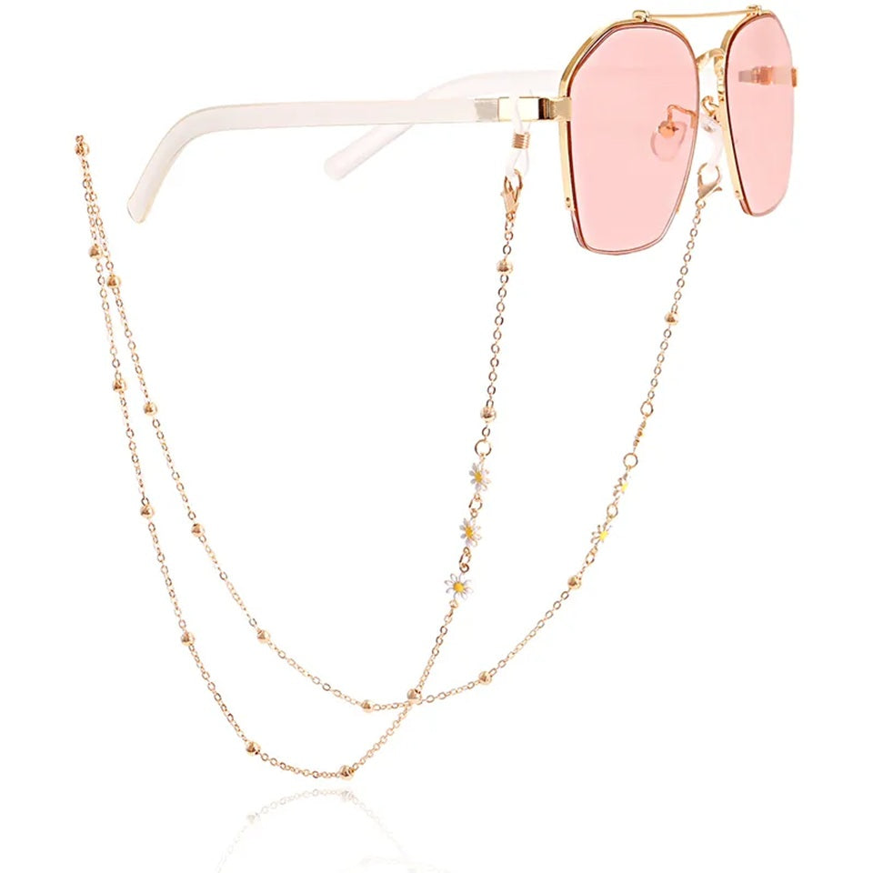 Chaîne de lunettes dorée ornée de petites marguerites blanches et de perles dorées, présentée accrochée à une paire de lunettes