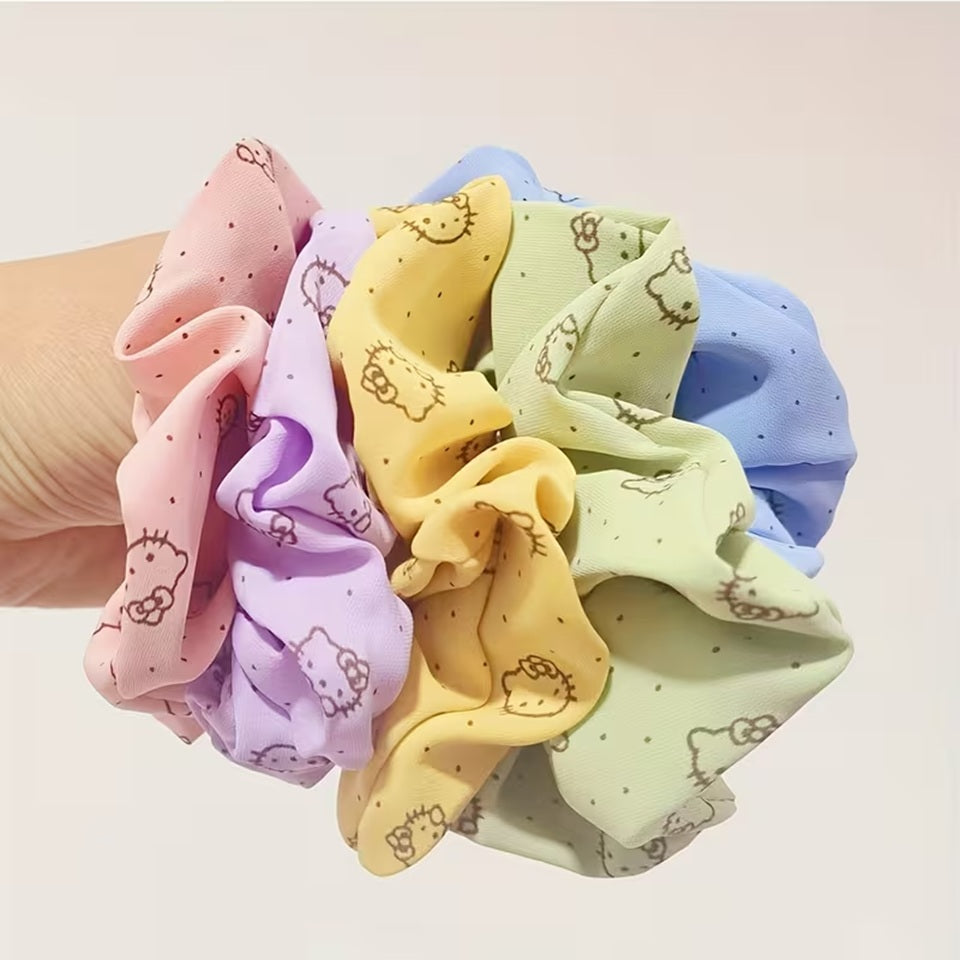 Lot de chouchous Hello Kitty colorés en tissu, tenus par une main de femme. Ces élastiques pour cheveux roses, jaunes, verts, bleus et violets apportent une touche mignonne et colorée aux coiffures du quotidien.
