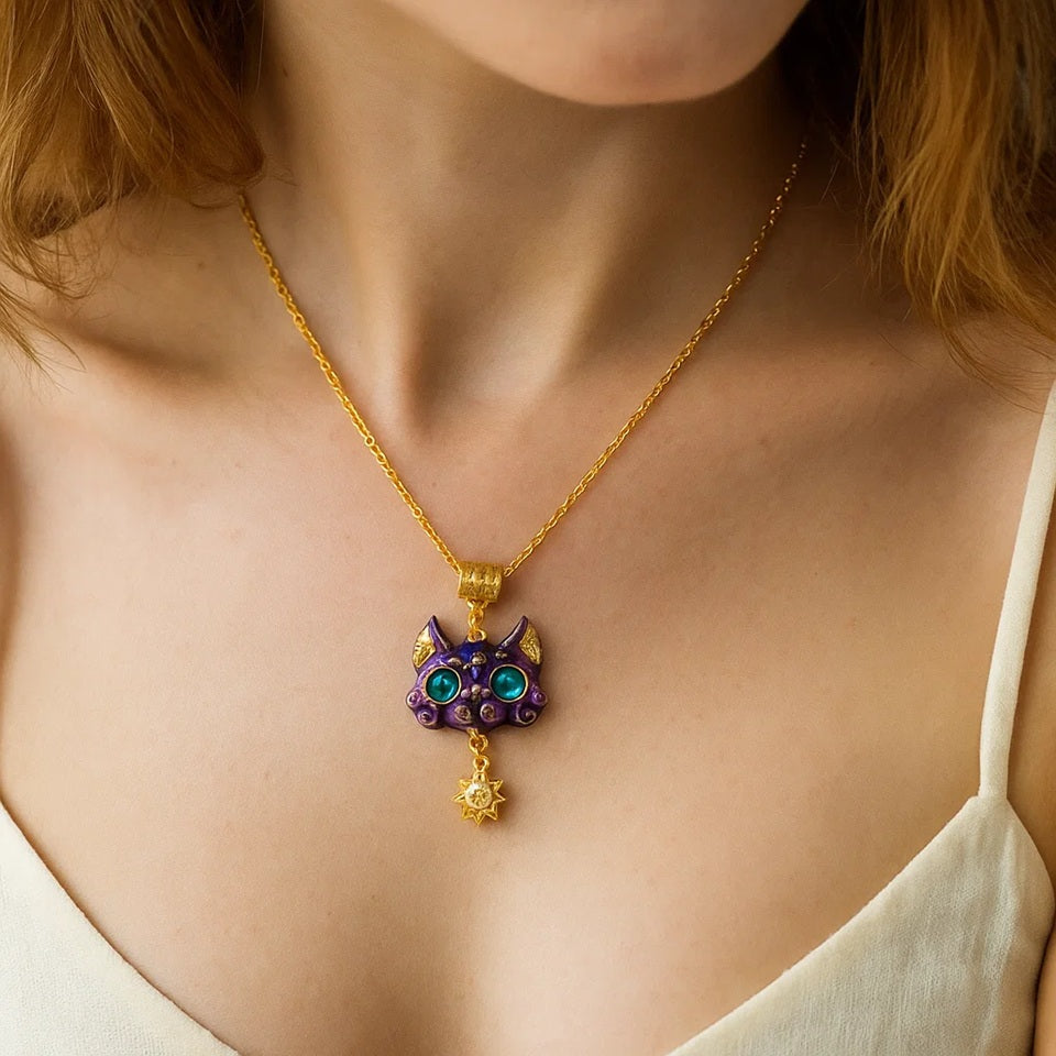 un collier doré dont le pendentif est un chat violet aux grands yeux bleus expressifs. Il a des décorations dorées comme une breloque en forme de soleil.