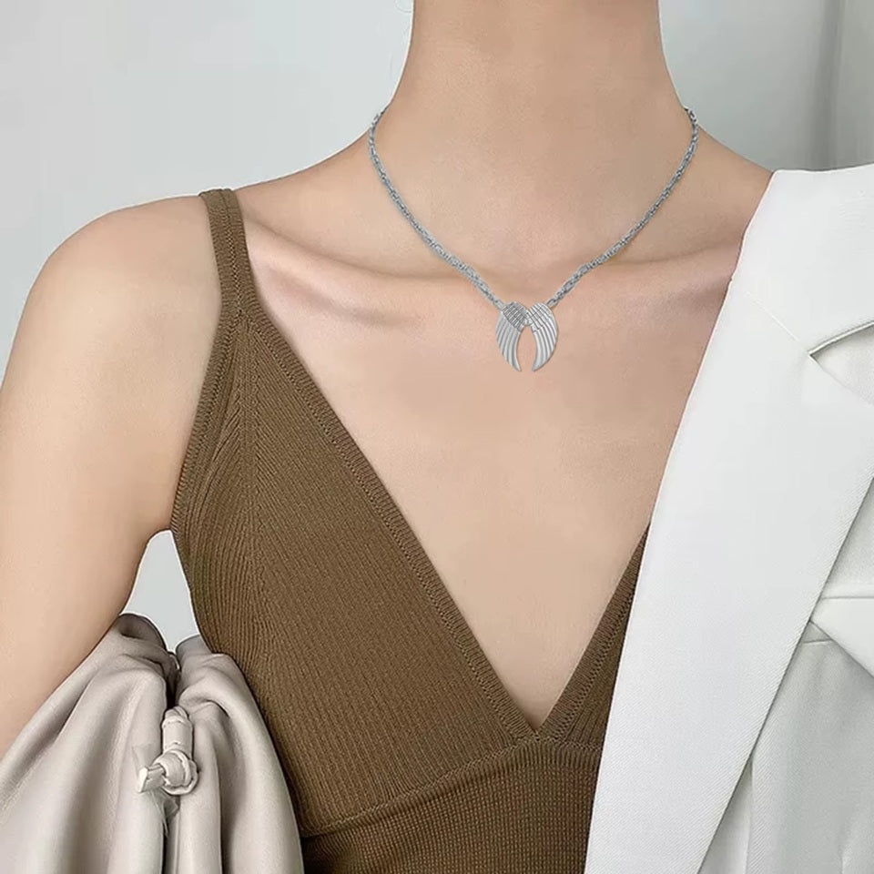un collier argenté dont le pendentif représente une paire d'ailes d'anges délicatement sculptées.