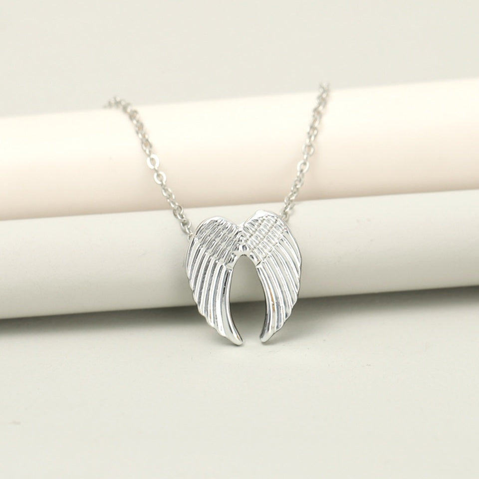 un collier argenté dont le pendentif représente une paire d'ailes d'anges délicatement sculptées.
