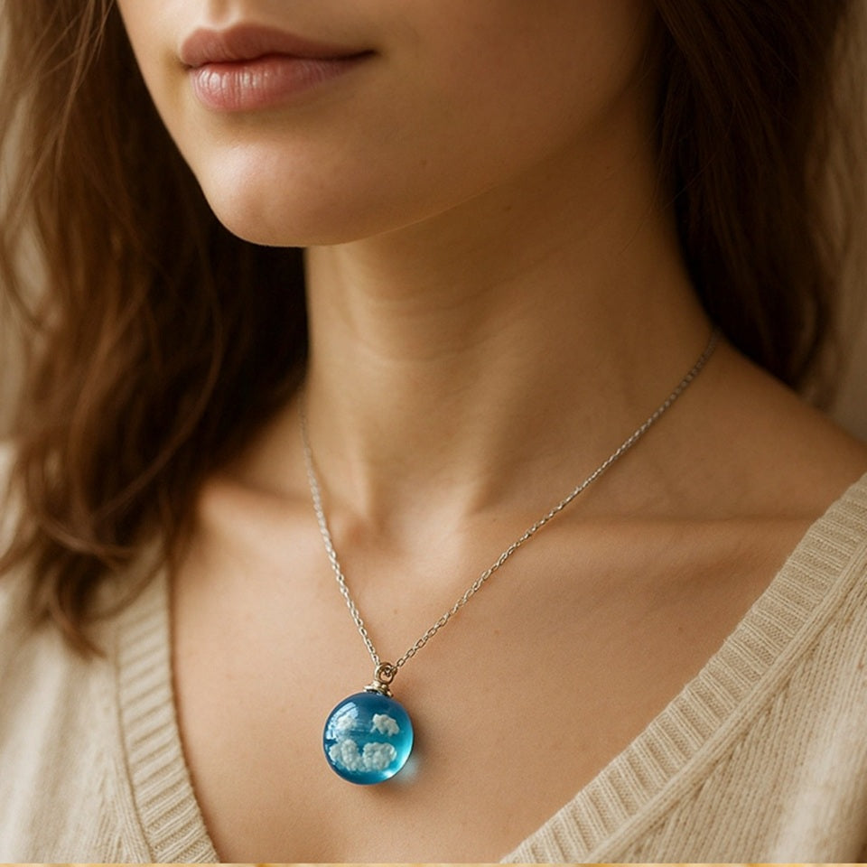 un joli collier argenté d'une sphÚre transparente et bleue renfermant des nuages comme si un bout d eciel y avait été capturé.