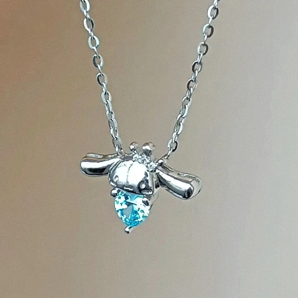 un superbe collier en alliage représentant Cinnamoroll, le petit chien de Sanrio qui tient un strass bleu en forme de coeur dans ses pattes. En coloris argenté, il apporte fraicheur et charme tout en discrétion.