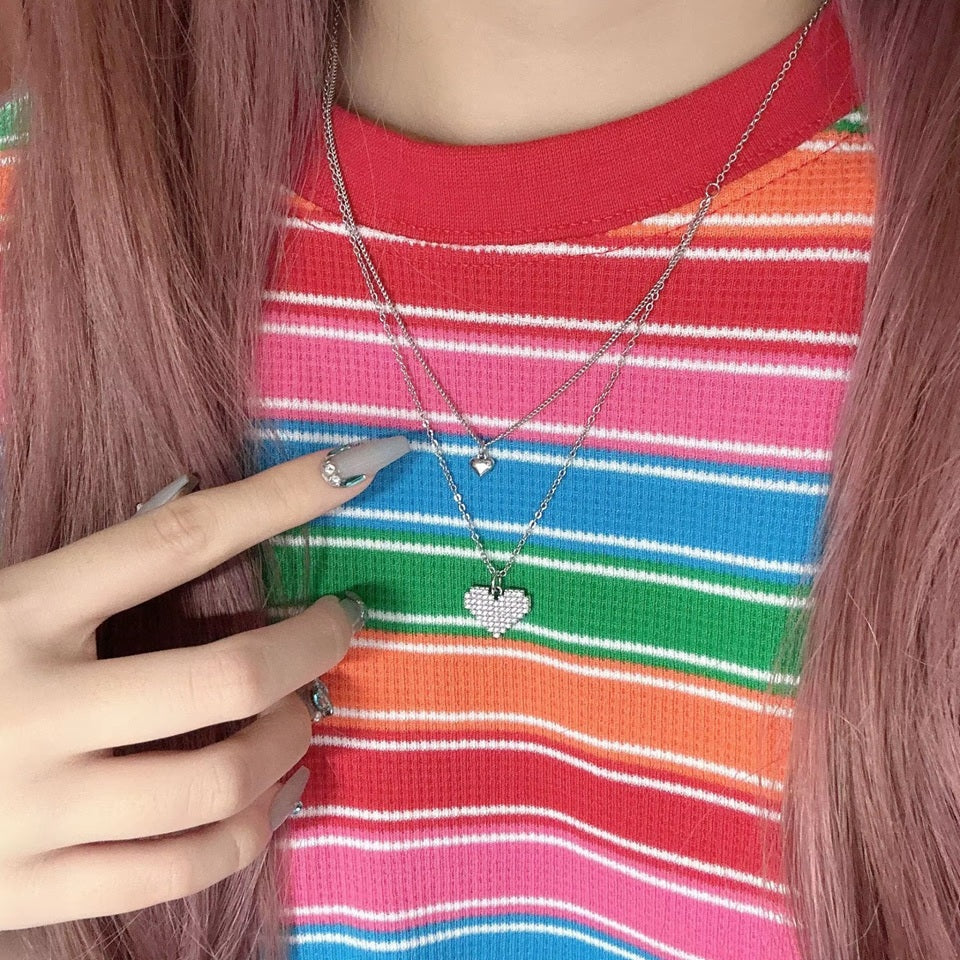 un collier composé de deux chaines reliées. Deux pendentifs en forme de coeur sont les chaines, dont un tout en strass brillants.