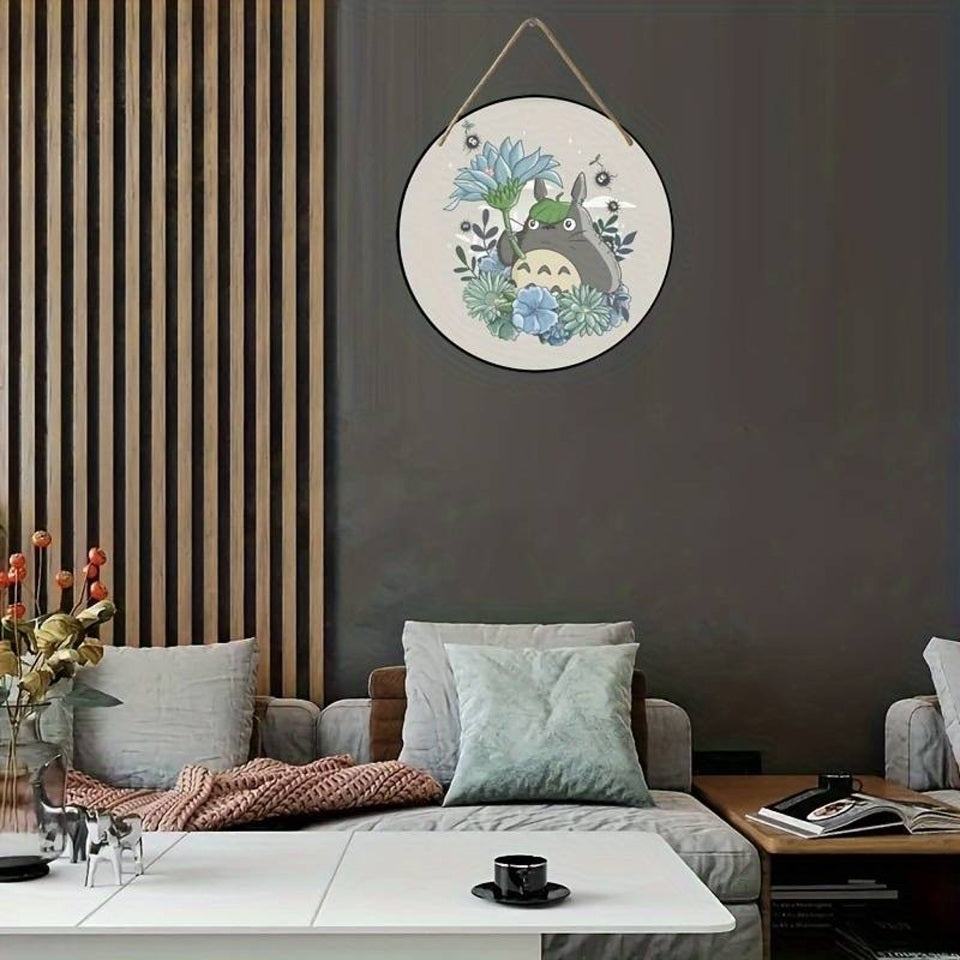 une décoration ronde au design de Totoro qui tient une jolie fleur. Il est entouré de fleurs. L'ensemble est délicat et tendre.