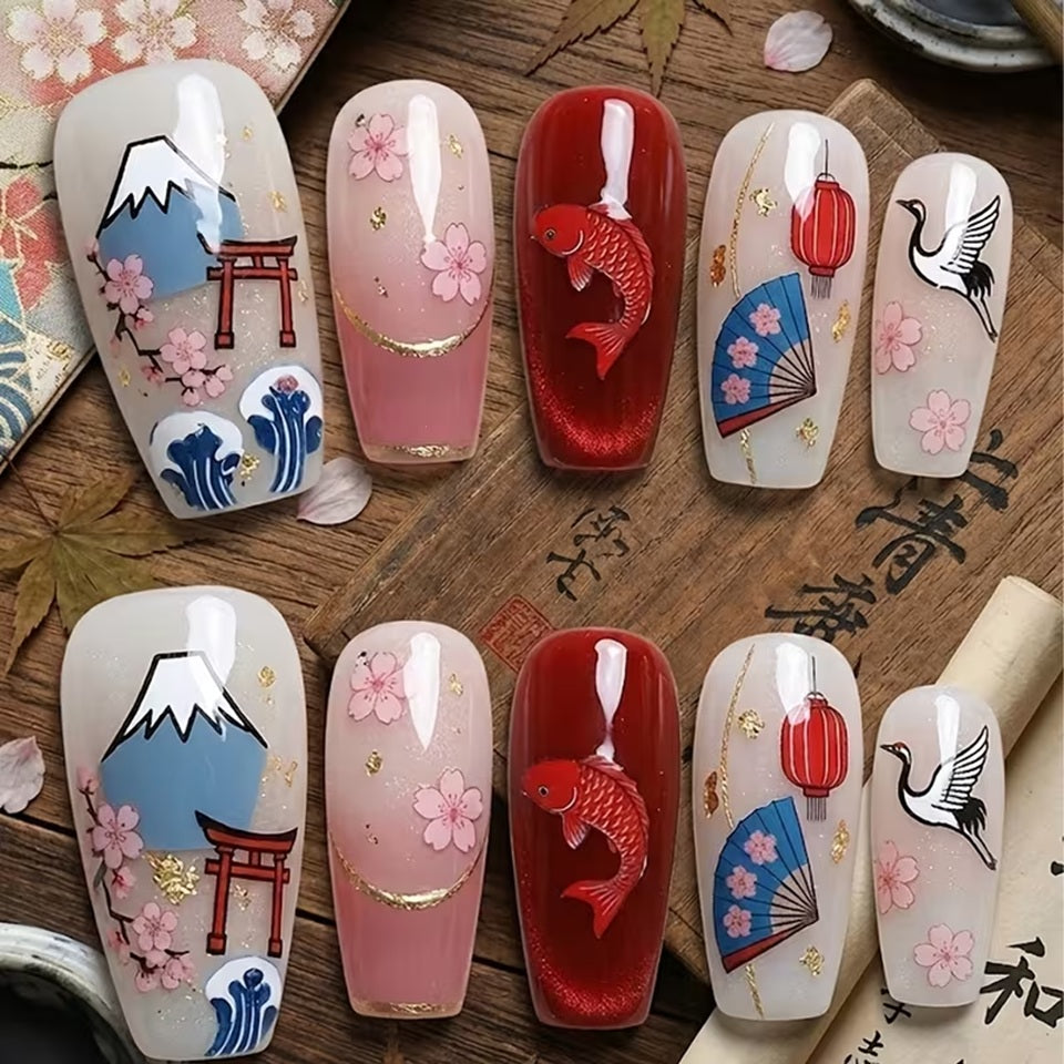 Des ongles vernis en rouge et blancs sur lesquels sont posés des stickers de nail art sur le thème du Japon : fleurs de sakura, carpe koi, éventail, tori et mont fuji.