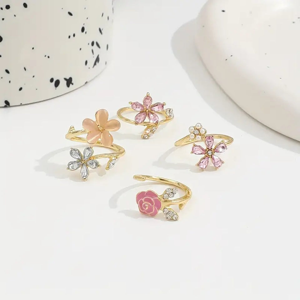 un ensemble de 4 bagues en alliage doré au design de fleurs roses élégantes et de strass brillants roses et argentés avec des perles. L'ensemble est romantique et féminin