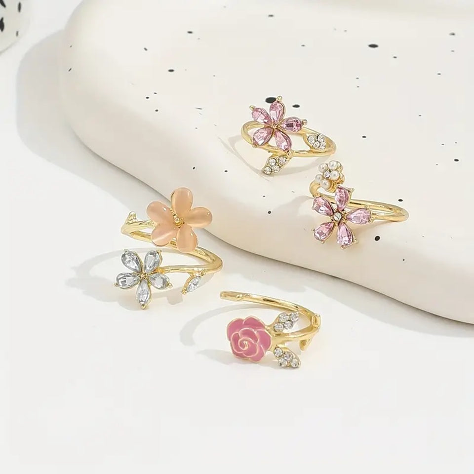 un ensemble de 4 bagues en alliage doré au design de fleurs roses élégantes et de strass brillants roses et argentés avec des perles. L'ensemble est romantique et féminin