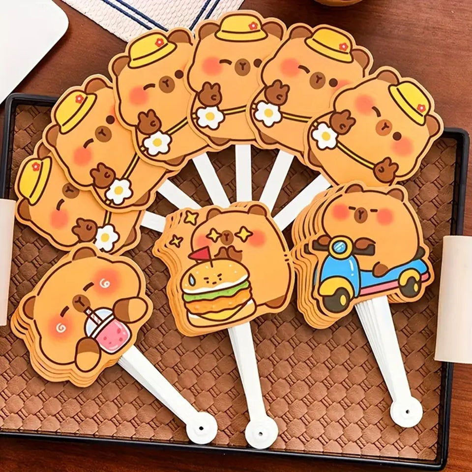 des éventails hyper rigolos et fun dont les lames sont des capybaras dans différentes situations amusantes : devant un hamburger, en scooter, en train de boire ou tout simplement content.