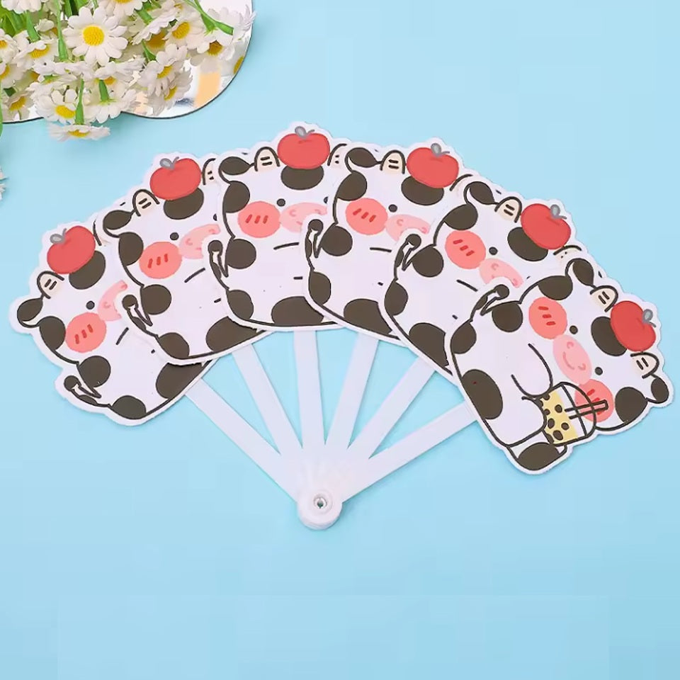 un éventail dont les lames représentent de mignonnes vaches noires et blanches qui boivent un bubble tea et qui ont une pomme rouge sur la tête. L'ensemble est adorale, c'est un accessoire utile et pratique pour les chaudes journées.