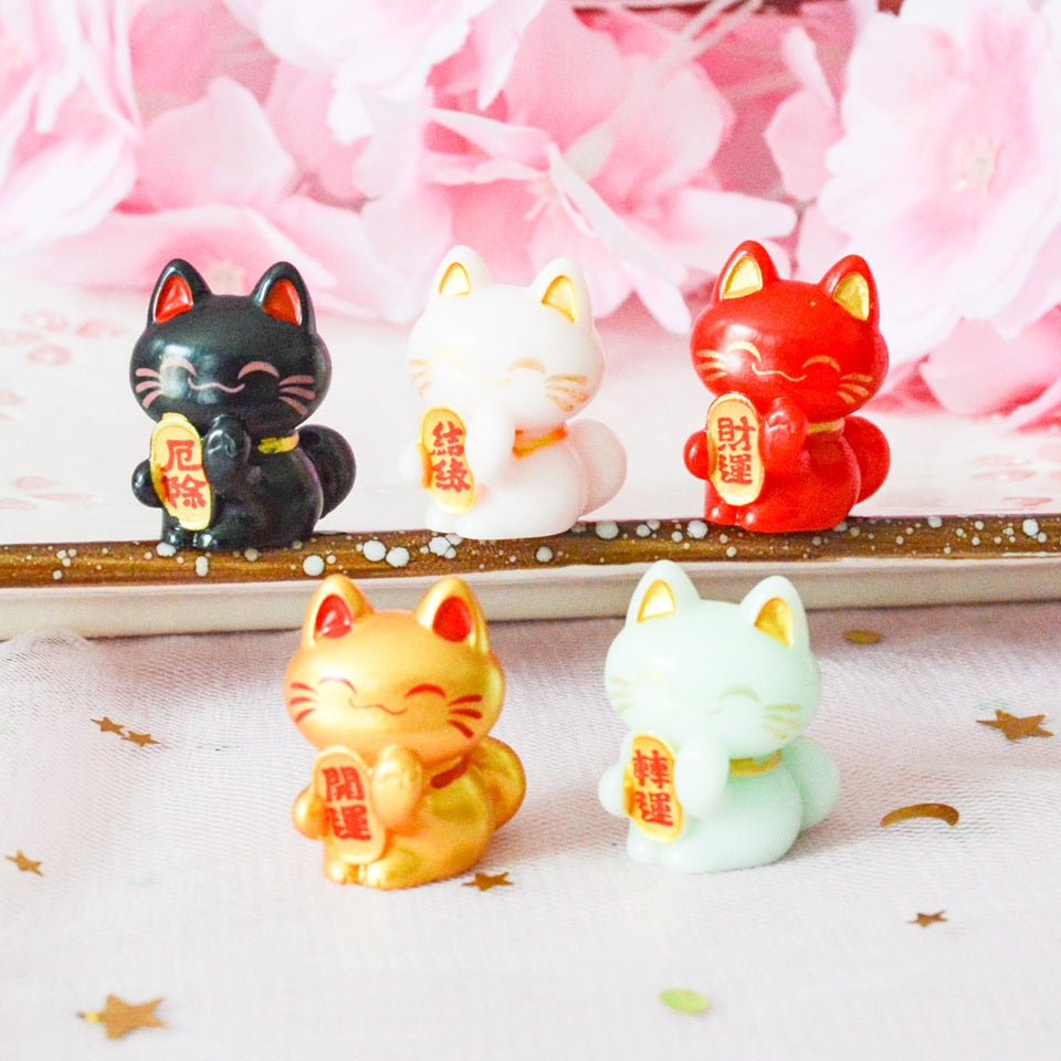 des petites figurines en forme de maneki neko de plusieurs couleurs différentes : jaune, blanc, vert, mauve, rouge, noir, rose, dorée et vert. Elles sont considérées comme porte-bonheur au Japon. Elles peuvent servir comme élément de décoration.