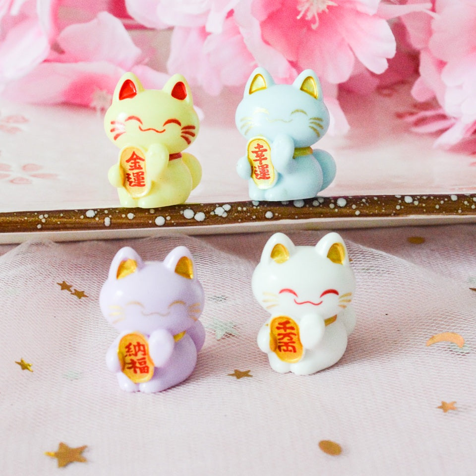 des petites figurines en forme de maneki neko de plusieurs couleurs différentes : jaune, blanc, vert, mauve, rouge, noir, rose, dorée et vert. Elles sont considérées comme porte-bonheur au Japon. Elles peuvent servir comme élément de décoration.