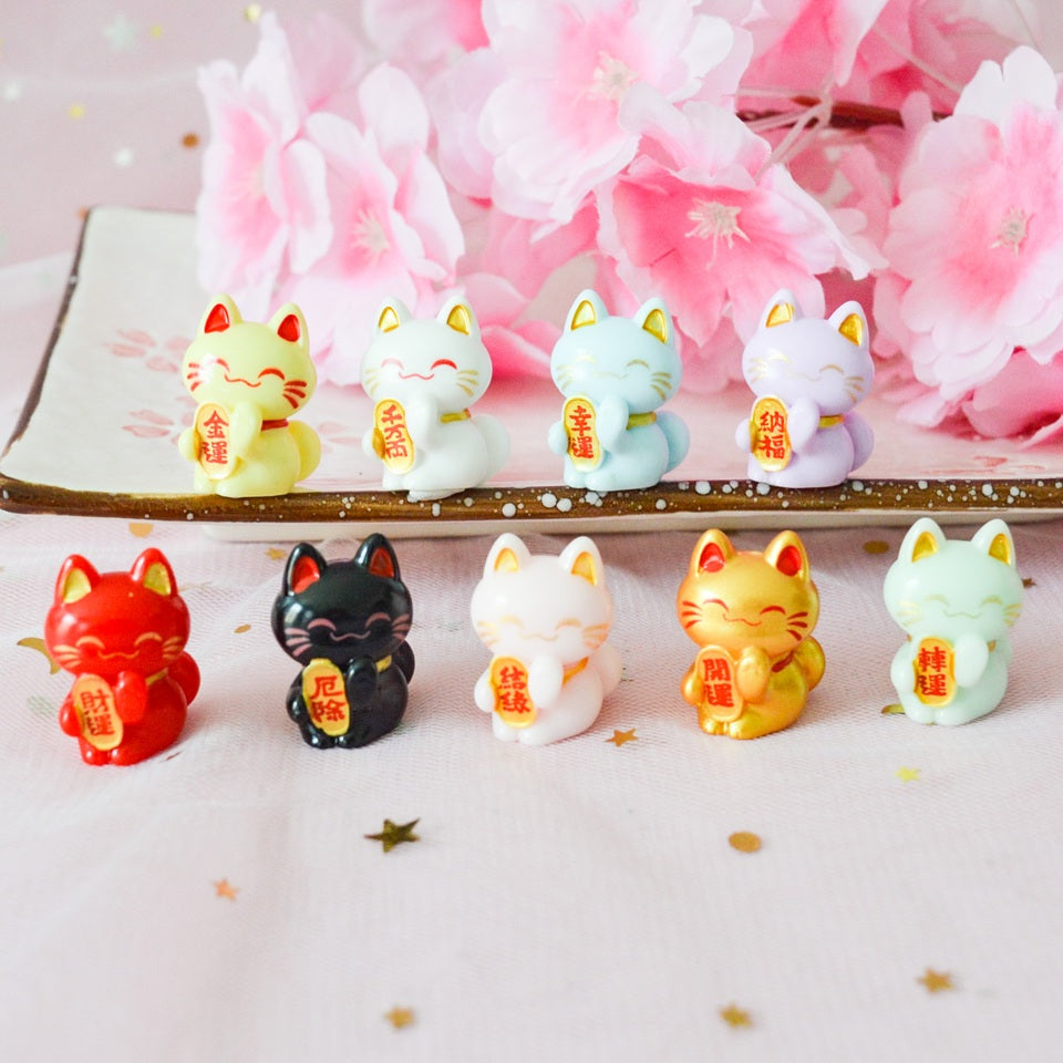 des petites figurines en forme de maneki neko de plusieurs couleurs différentes : jaune, blanc, vert, mauve, rouge, noir, rose, dorée et vert. Elles sont considérées comme porte-bonheur au Japon. Elles peuvent servir comme élément de décoration.