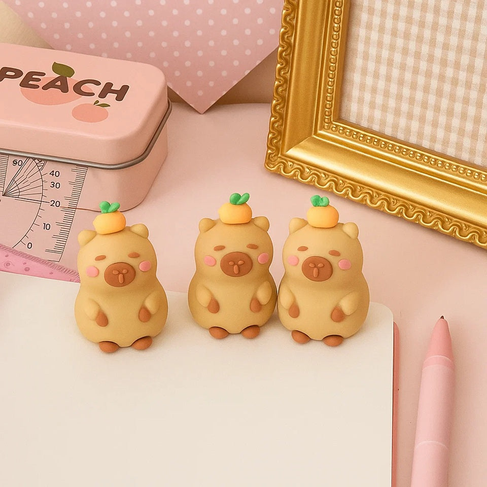 une adorable gomme en forme de capybara. Une petite orange est posée sur sa tête. L'ensemble est amusant et mignon.