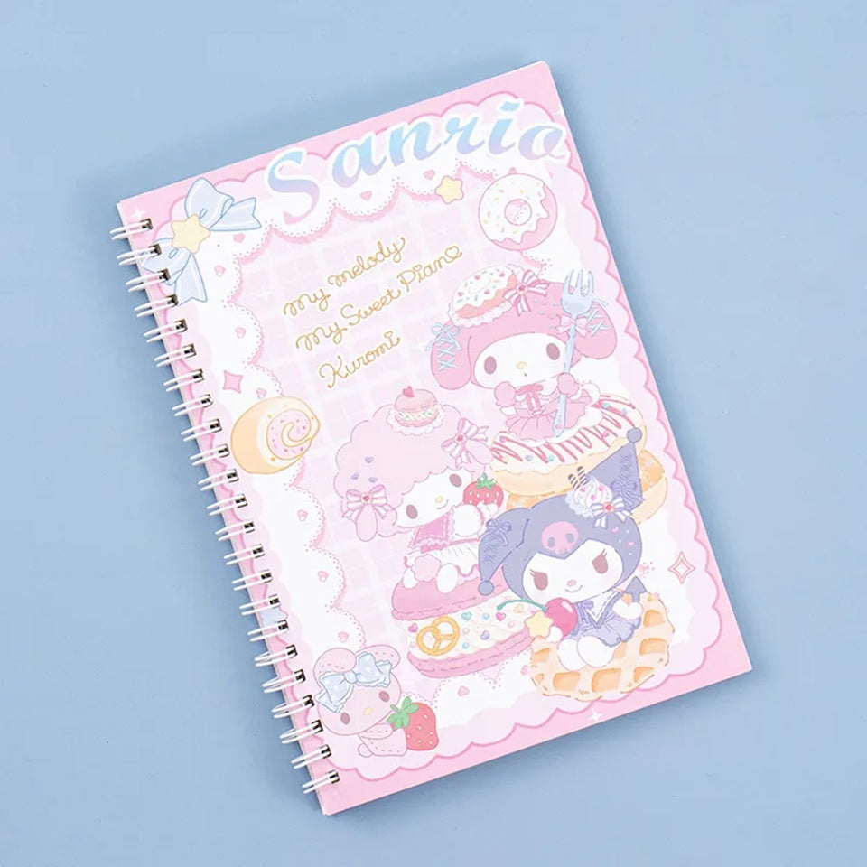 un grand carnet à spirales Sanrio mettant en scène Kuromi, My Melody et My sweet piano. Elles sont sur une gaufre, un macaron et un donut L'ensemble est hyper gourmand et kawaii dans les tons de rose blanc et bleu
