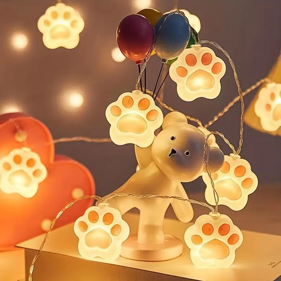 une guirlande LED en forme de pattes de chat roses toutes mignonnes. Elle diffuse une lumière jaune douce et chaleureuse. Idéal pour un coin cocooning.