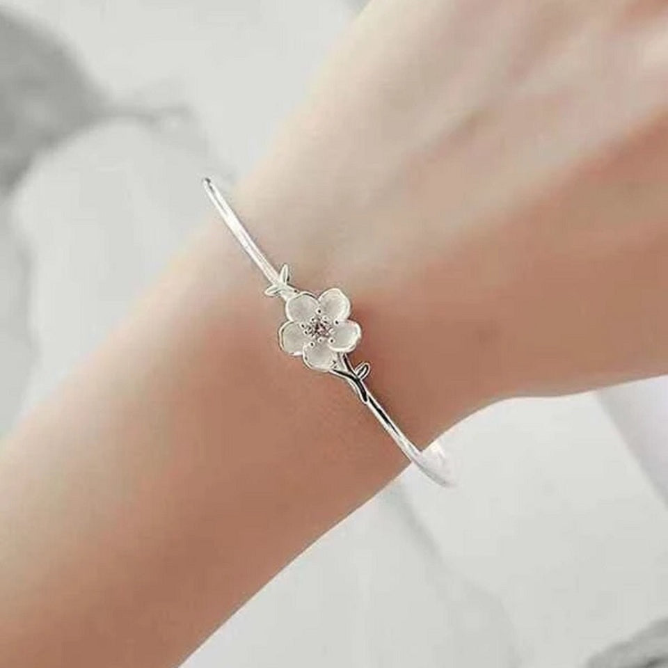 un superbe jonc argenté rigide sur lequel trône une jolie fleur de prunier, un strass rose repose en son coeur.