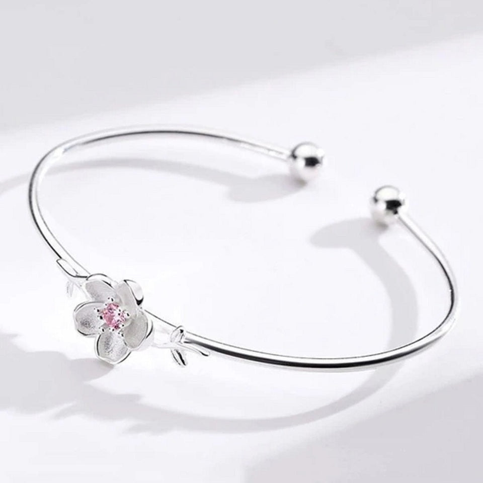 un superbe jonc argenté rigide sur lequel trône une jolie fleur de prunier, un strass rose repose en son coeur.