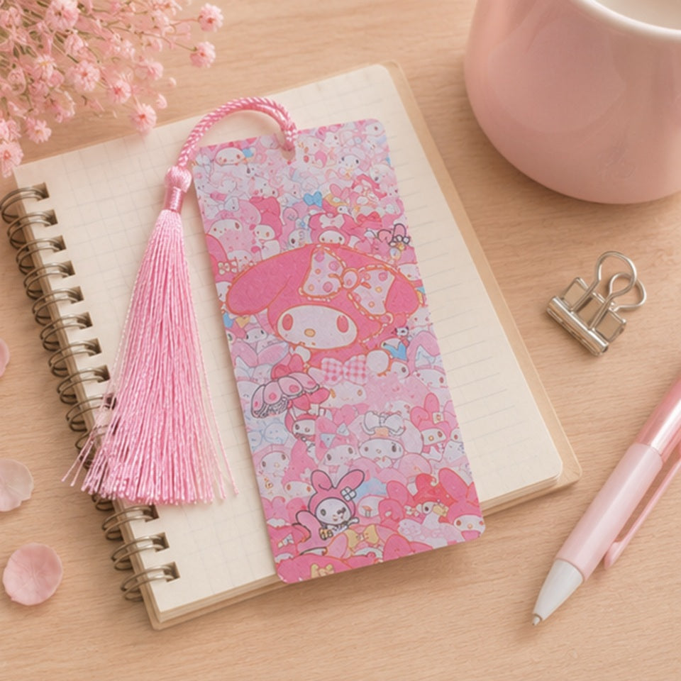 Marque-page kawaii My Melody rose avec pompon assorti, présenté sur un carnet dans un décor pastel. Accessoire de lecture Sanrio mignon et original pour accompagner livres et romans.