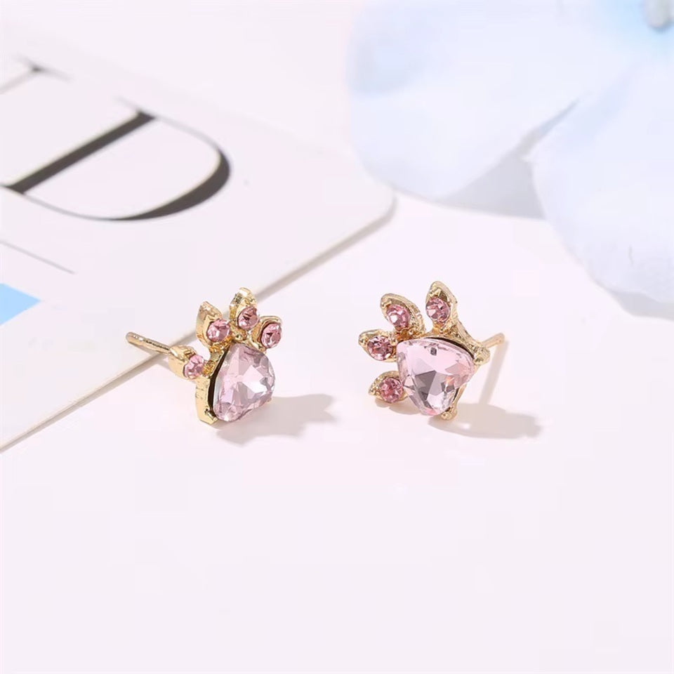 une parure de bijoux composée d'un collier, d'un bracelet, d'une bague et de boucles d'oreilles en forme de patte de chat tout en strass rose.