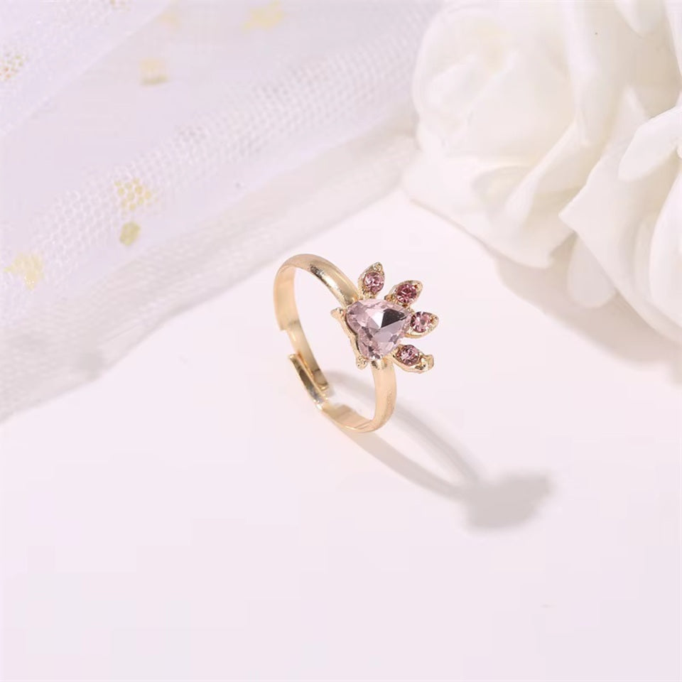 une parure de bijoux composée d'un collier, d'un bracelet, d'une bague et de boucles d'oreilles en forme de patte de chat tout en strass rose.