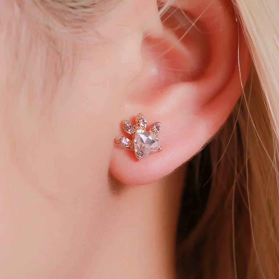une parure de bijoux composée d'un collier, d'un bracelet, d'une bague et de boucles d'oreilles en forme de patte de chat tout en strass rose.