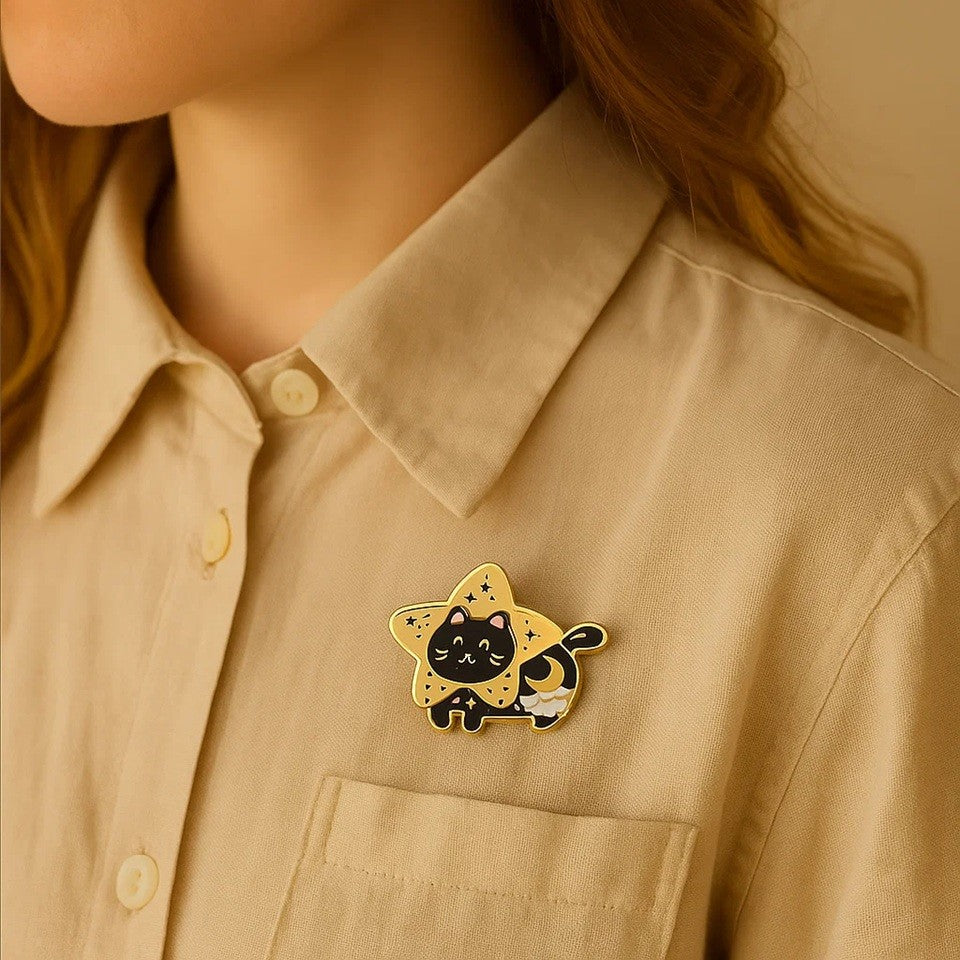 un pin's doré en forme d'un chat noir bien dodu et tout mignon dans la fourrure est ornée d'un croissant de lune et d'un nuage. Il a la tête dans une grande étoile dorée.