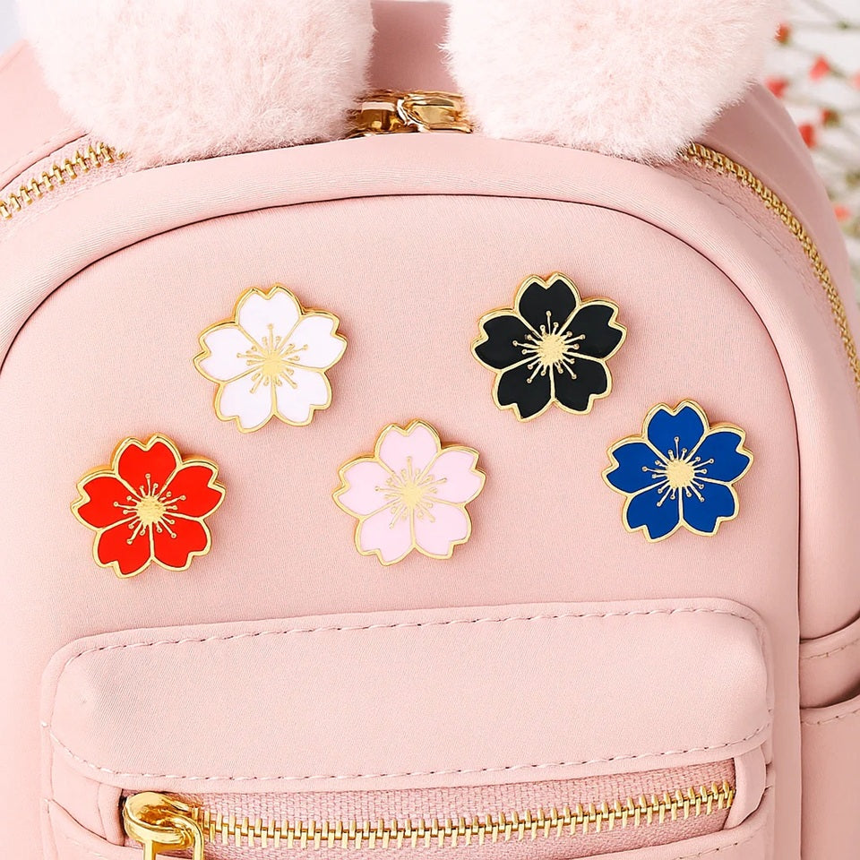 des pin's en forme de fleur de sakura colorée : noir, rouge, bleu, blanc et rose. Avec leur finition dorée, ils sont symbole de renouveau et de beauté.
