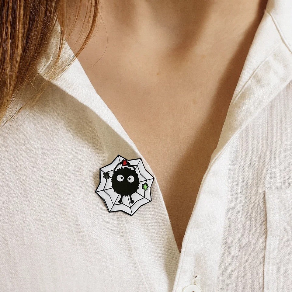 un pin's en forme de noiraude tiér des films Ghibli : le voyage de Chihiro et Mon voisin Totoro. La noriaude lève un morceau de sucre et elle est sur un fond en forme de toile.