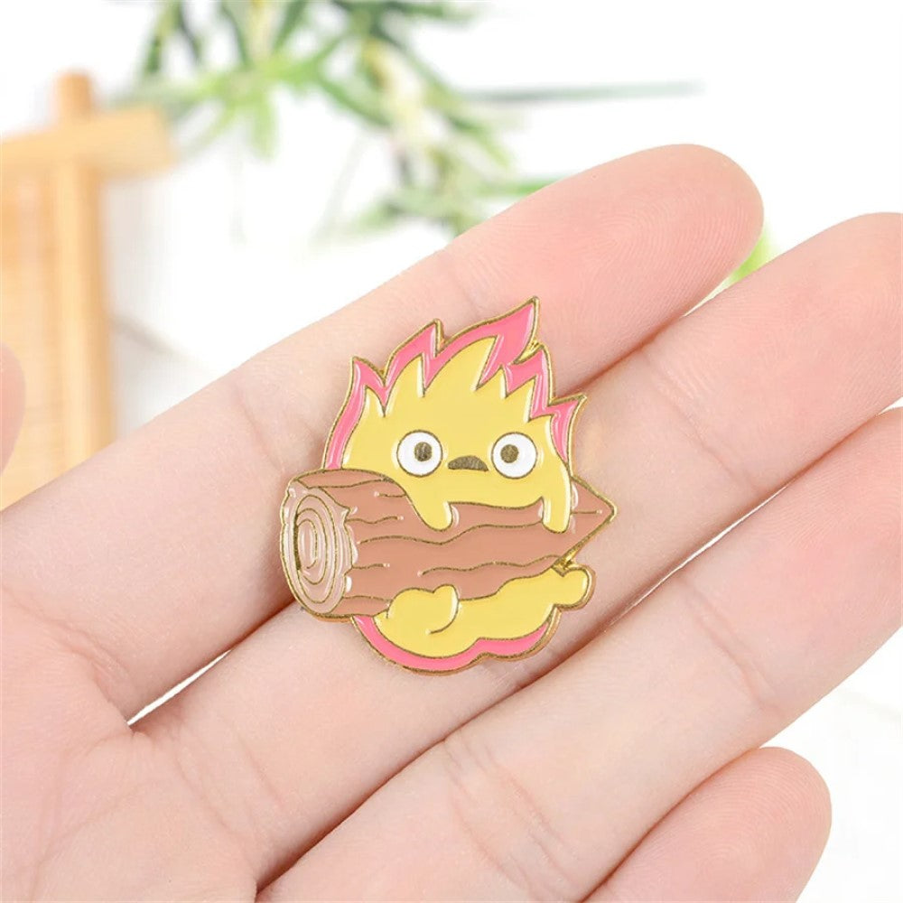 un adorable pin's représentant Calcifer le personnage du château ambulant tenant une buche de bois tenue dans la main. Ambiance calme et nature. Idéal à collectionner.