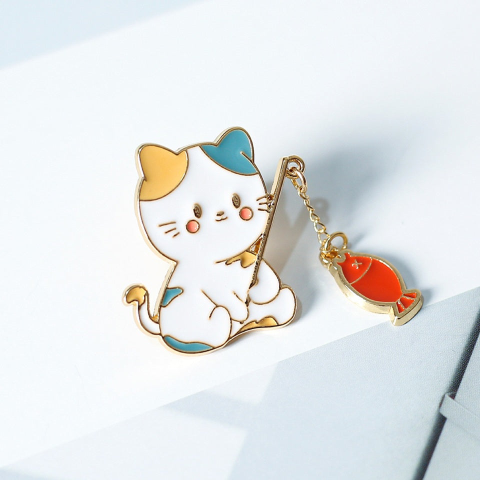 un pin's en forme de chat qui est en train de pêcher. Il a une canne à pêche composée d'une chainette. Au bout se trouve un poisson !