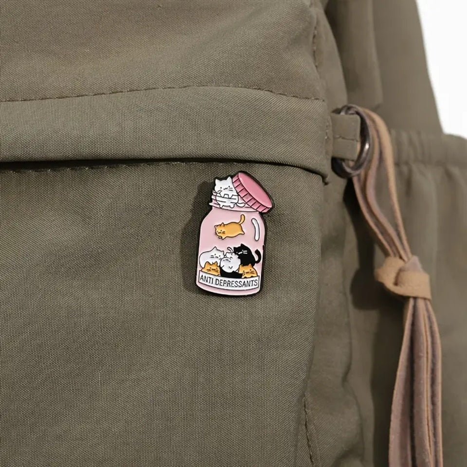 un pin's en forme de bocal dans lequel se trouve plein de petits chats colorés. Sur la boite est inscrit antidepressants, comme si les petits chats étaient un remède contre la morosité