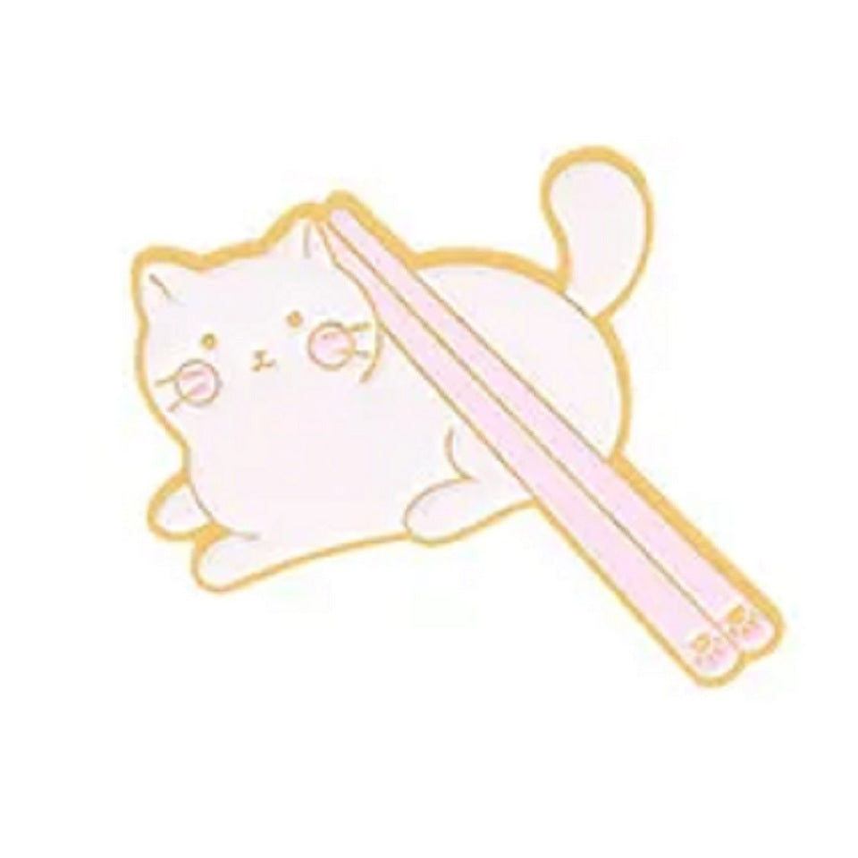 un adorable pin's en forme de chat blanc sur lequel repose une paire de baguettes au motif de patte de chat.