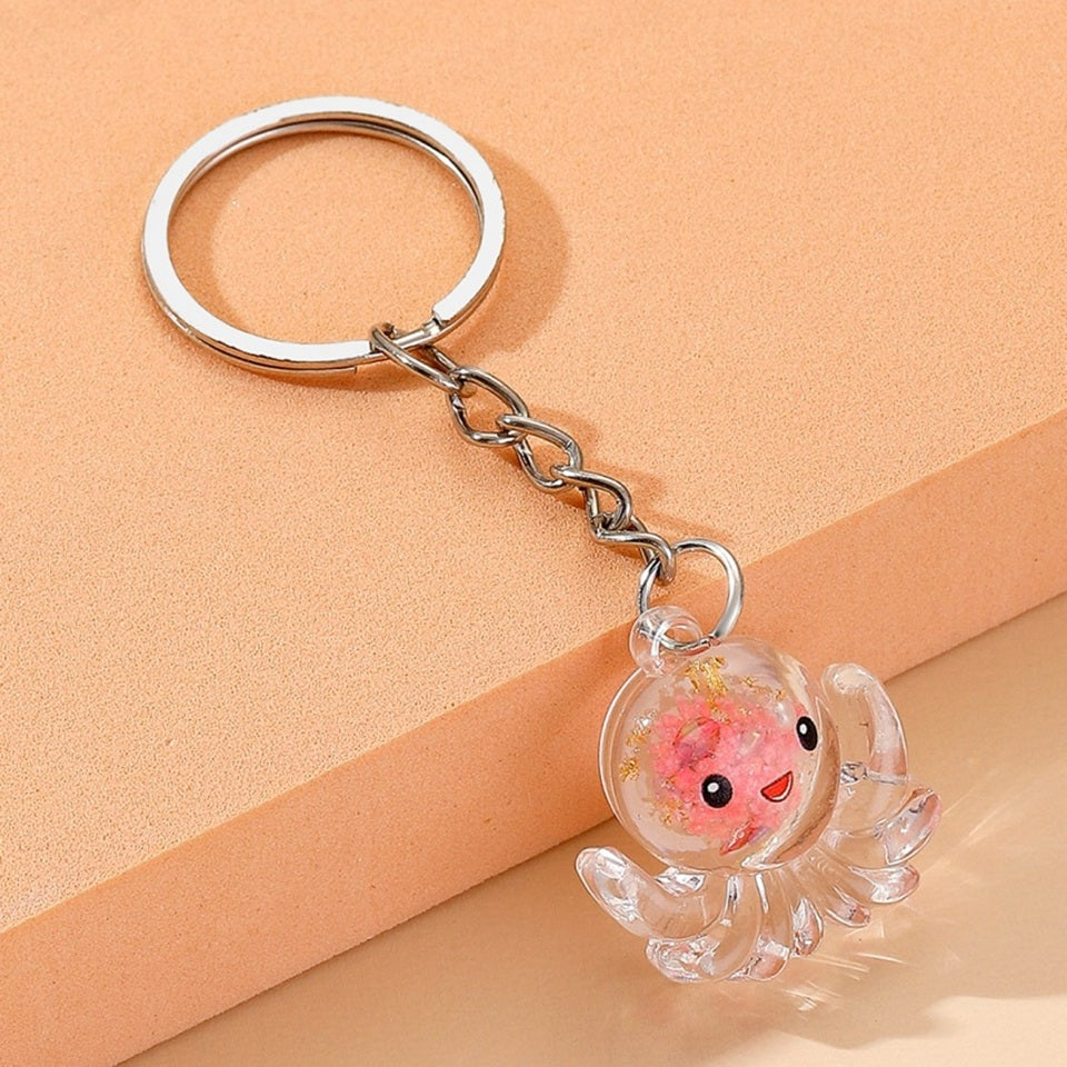 un porte-clé en acrylique en forme d'octopus trop mignon. Il renferme des paillettes roses et dorées et a une expression kawaii trop mignonne !