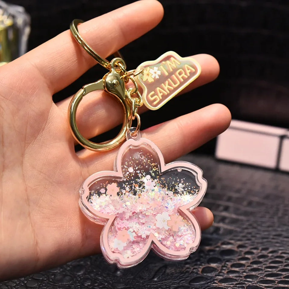 un porte-clés en forme de fleur de sakura rose dans lequel se trouve des paillettes en forme de fleurs façon quicksand. L'ensemble est poétique et magique.