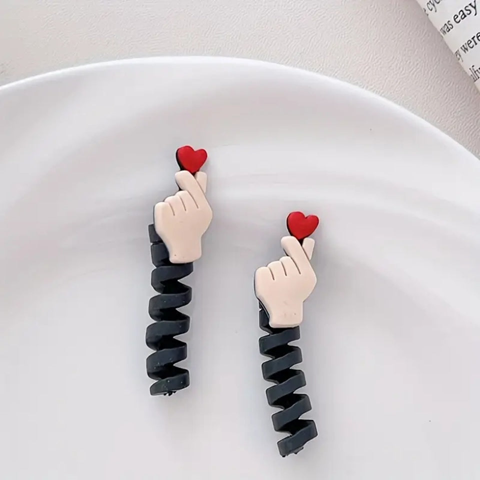 un protège câble en forme de mains qui forment un cœur, le finger heart coréen accompagné d'un joli cœur rouge. Idéal pour protéger et allonger la durée de vie de vos câbles