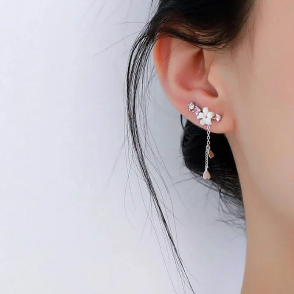 une paire de boucles d'oreilles qui épousent le lobe de l'oreille avec délicatesse et élégance. Une jolie fleur de sakura blanche et des strass blancs et roses viennent embellir l'ensemble. ne petite chaine pendante ornée de pétale de sakura est suspendue aux boucles.