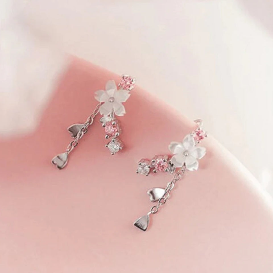 une paire de boucles d'oreilles qui épousent le lobe de l'oreille avec délicatesse et élégance. Une jolie fleur de sakura blanche et des strass blancs et roses viennent embellir l'ensemble. ne petite chaine pendante ornée de pétale de sakura est suspendue aux boucles.