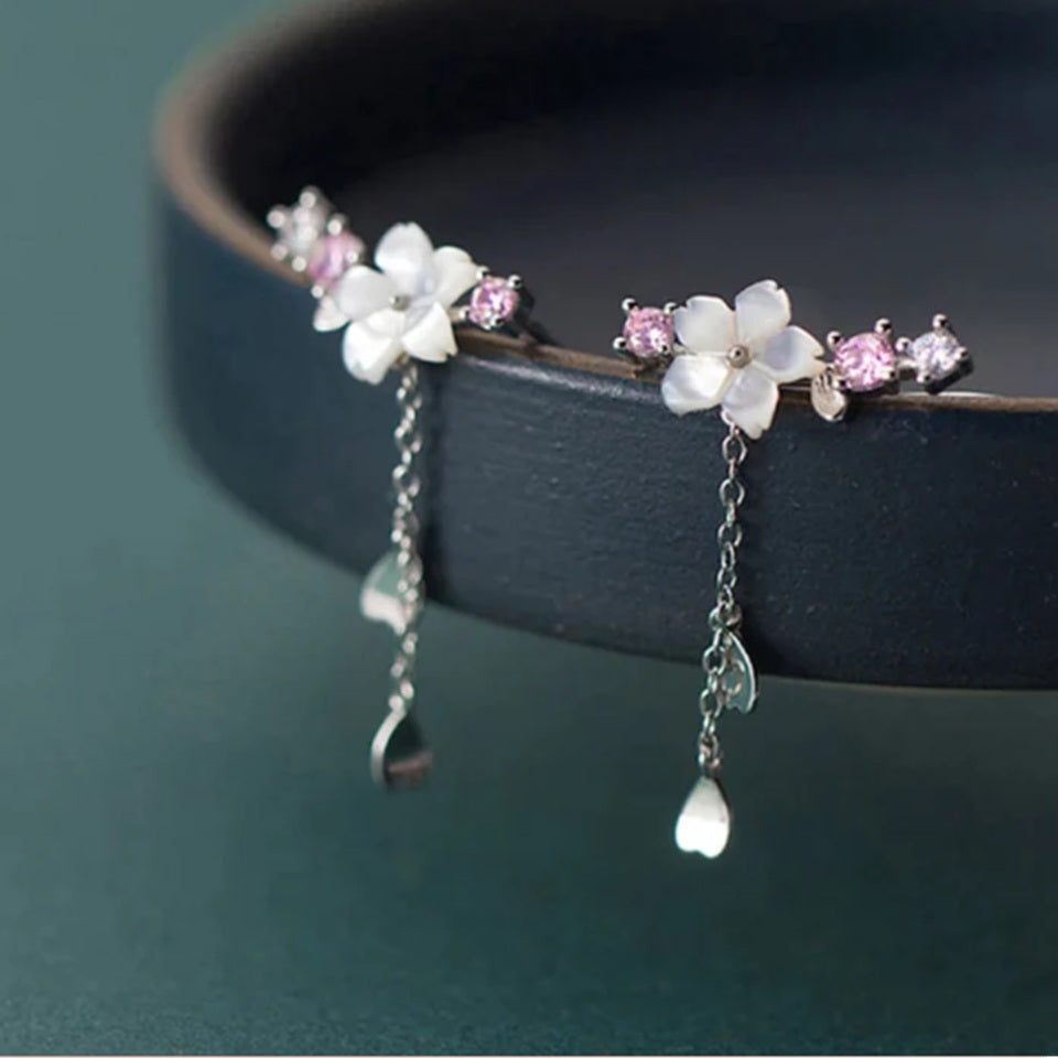une paire de boucles d'oreilles qui épousent le lobe de l'oreille avec délicatesse et élégance. Une jolie fleur de sakura blanche et des strass blancs et roses viennent embellir l'ensemble. ne petite chaine pendante ornée de pétale de sakura est suspendue aux boucles.