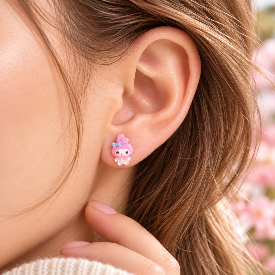 Petite puce d’oreille My Melody rose kawaii portée à l’oreille, avec personnage entier et nœud bleu, dans un décor doux et fleuri.