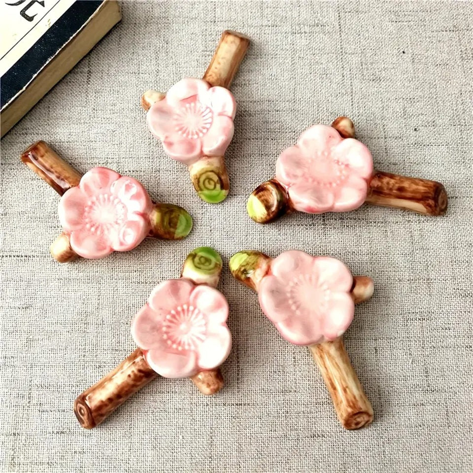 un repose baguette en céramique en forme d'une branche de cerisier sur laquelle est posé une délicate fleur de sakura rose. Idéal pour embellir et décorer une table