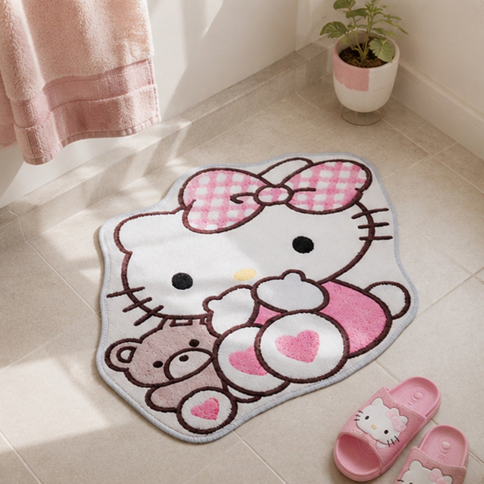 Tapis de sol en forme de Hello Kitty tenant un ourson, dans des tons blanc, rose pastel et gris clair, posé sur un tapis moelleux crème dans une chambre d'enfant lumineuse. Autour du tapis se trouvent un pouf rond rose, une peluche Hello Kitty et un meuble en bois clair avec des rangements roses, créant une ambiance douce, kawaii et chaleureuse.