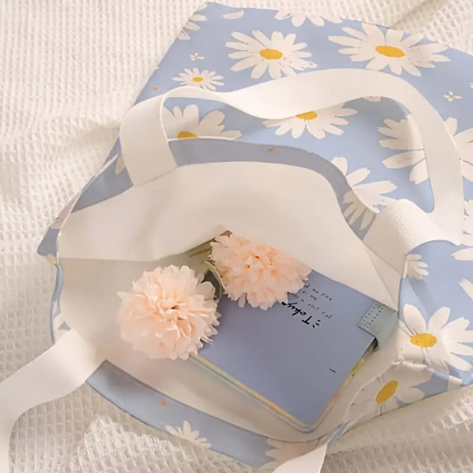 un tote bag en polyester au motif de marguerites blanches sur un fond bleu ciel. Avec ses deux anses blanches, il est pratique pour transporter tous les essentiels.