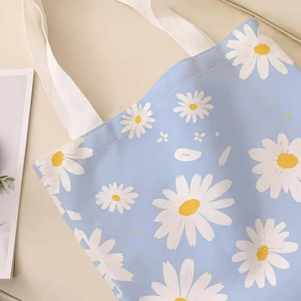 un tote bag en polyester au motif de marguerites blanches sur un fond bleu ciel. Avec ses deux anses blanches, il est pratique pour transporter tous les essentiels.