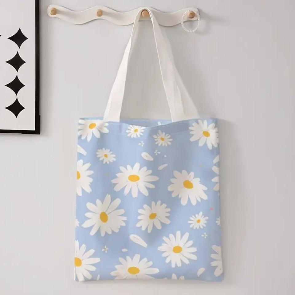 un tote bag en polyester au motif de marguerites blanches sur un fond bleu ciel. Avec ses deux anses blanches, il est pratique pour transporter tous les essentiels.