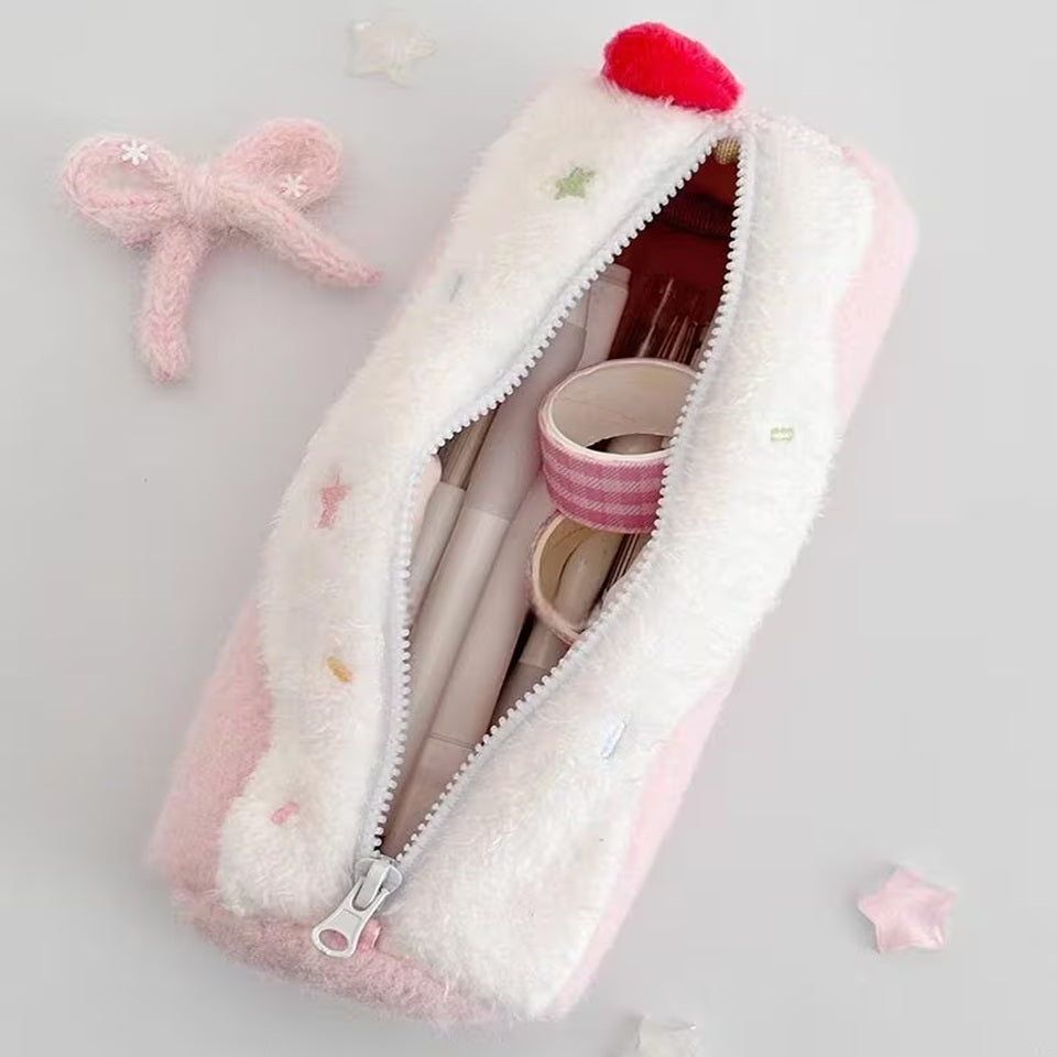 Une trousse en peluche kawaii rose pastel posée sur une bureau blanc, entouré d'éléments kawaii. Elle est entrouverte et laisse apparaitre diverses fournitures de papeterie. Atmosphère chaleureuse, féminine et mignonne, idéale pour une présentation de fournitures de papeterie