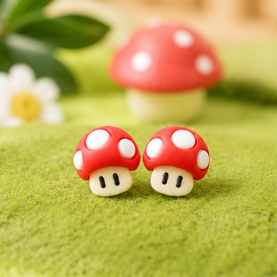 une paire de boucles d'oreilles en forme de champignon rouge à pois blancs, inspirées du jeu vidéo Mario.