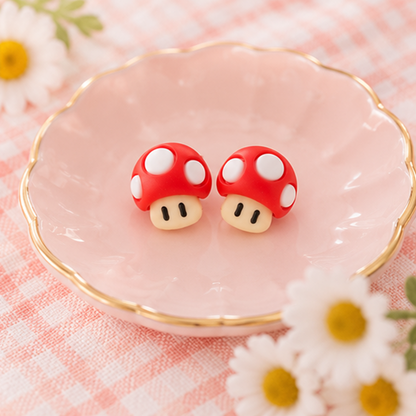 une paire de boucles d'oreilles en forme de champignon rouge à pois blancs, inspirées du jeu vidéo Mario.