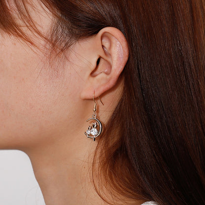 une paire de boucles d'oreilles en forme de lune dorée sur laquelle reposent deux adorables chats dont le corps est en strass brillant